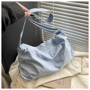 Gros plan sur le sac bandoulière en nylon bleu clair avec détails de plis à cordon latéral