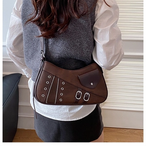 Detail of vintage brown leather underarm bag with metal grommets and buckles worn by model