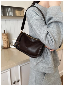 Detailed macro view of dark brown leather shoulder bag with gold zipper and embossed logo