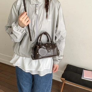 Detail der dunkelbraunen Boston Bag mit silbernen Sternnieten und Herzanhänger am Model