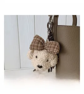 Close-up of fluffy white poodle bag charm with a brown plaid bow on a leather bag