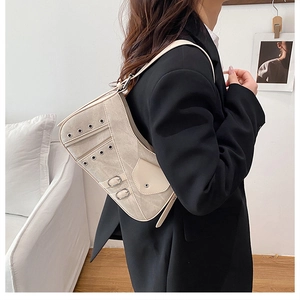 Detailed side view of a beige saddle underarm bag with silver hardware on a female model