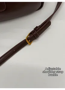 Detail of dark brown leather bag showing golden buckle and adjustable shoulder strap