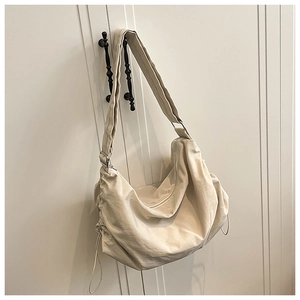 Détail du sac besace en nylon crème avec large bandoulière et fermeture à cordon