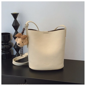 Detail of cream white bucket bag with pebble leather texture and cute teddy bear charm