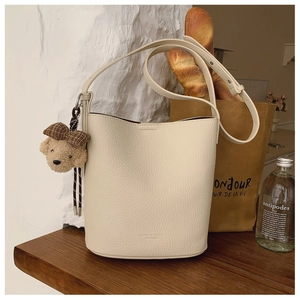 Close-up of off-white lychee leather bucket bag with cute plush bear and bow keychain