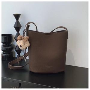 Detail of dark brown lychee leather bucket bag with matching strap and plush bear charm