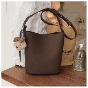 Detail of dark brown lychee leather bucket bag with a plush bear charm in a French setting