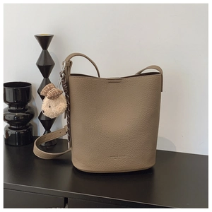 Detail of khaki pebbled leather bucket bag with braided strap and cute bear charm