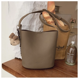 Detailed macro of khaki bucket bag showing lychee grain texture and bear charm