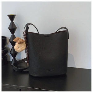 Detail of black lychee grain leather bucket bag with a cute plush bear charm accessory