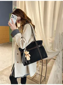 Close-up of black tote bag with brown leather straps and cute plush bear charm