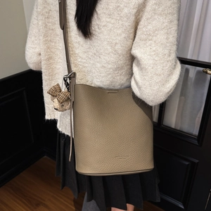Close-up of taupe litchi grain leather bucket bag featuring a cute teddy bear charm