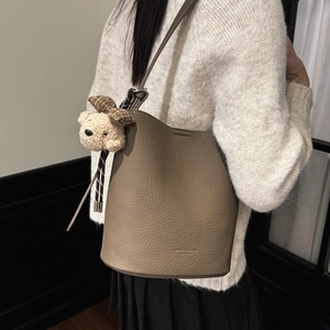 Detail of brown pebbled leather bucket bag with cute bear charm and logo embossing