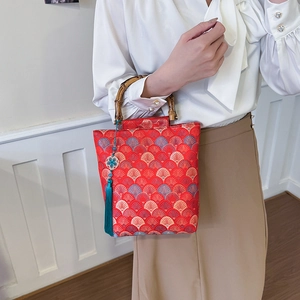 Detail of red jacquard handbag with bamboo handle and blue tassel on a white background