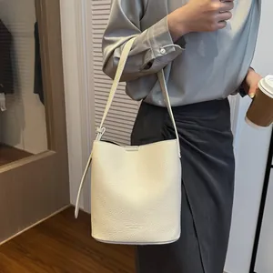 Detail of white lychee leather bucket bag featuring MINT & SAGE logo and thin strap