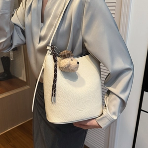 Detail of warm white bucket bag with pebble leather, plush dog charm and woven pendant
