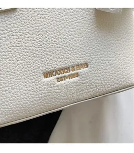 Close-up of white pebble grain leather shoulder bag featuring a gold embossed logo