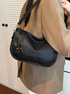 Minimalist black crescent shoulder bag with metallic tassels worn by model in suit