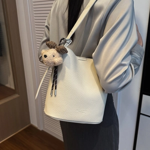 Detail of white litchi pattern leather bucket bag with cute bear charm and shoulder strap