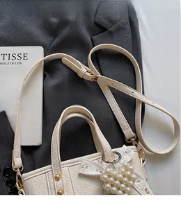 Detail of cream bucket bag with lychee grain texture and pearl heart charm on a grey suit