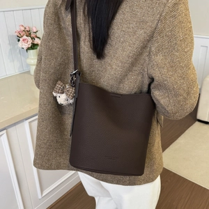 Detail of dark brown pebble leather bucket bag with cute bear charm and long shoulder strap