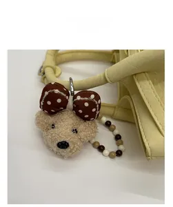 Detail of teddy bear plush charm with bead strap on a textured yellow bucket bag
