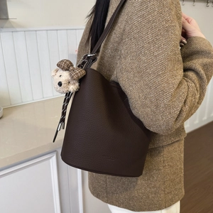 Detail of dark brown lychee leather bucket bag featuring a plush bear and bow charm