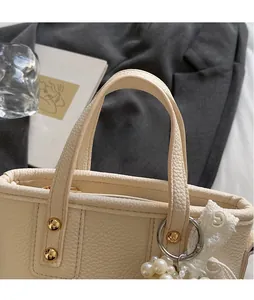 Detail of cream bucket bag with gold rivets and elegant pearl lace charm accent