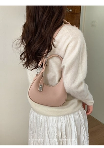 Chic pink crescent-shaped shoulder bag with litchi grain texture worn by a model