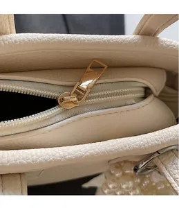 Detail of smooth gold zipper on beige lychee grain leather bag with pearl accent