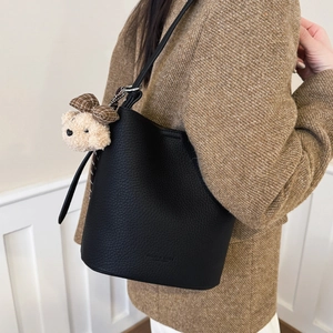 Detail of black lychee grain bucket bag featuring a plush bear charm and embossed logo