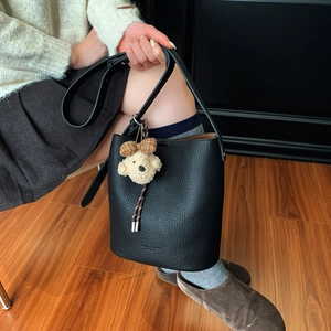 Close-up of black lychee grain leather bucket bag with a cute plaid bow plush bear charm