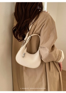 Detail of minimalist cream leather crescent bag with silver twist lock and trench coat styling