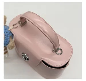 Detail of pink box bag featuring a rounded handle, metal lock, and a cute teddy bear charm