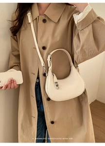 Close-up of cream lychee-grain crescent bag worn with a chic trench coat and metal lock