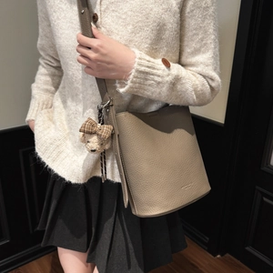Retro beige leather bucket bag with bear pendant shown on model in stylish indoor setting