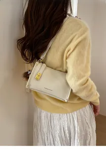 Detail of minimalist cream leather crossbody bag with gold buckle and fuzzy charm