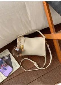 Detail of cream beige crossbody bag with litchi grain and cute plush toy charm