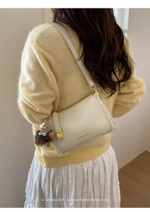 Detail of cream white leather handbag with gold lock and brown plush charm on a model