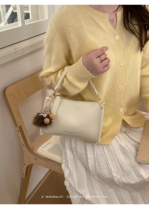 Detail of cream-colored litchi grain leather handbag with gold zipper and plush charm