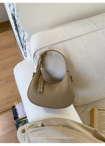 Close-up of khaki crescent bag with pebble leather and silver twist lock on sofa