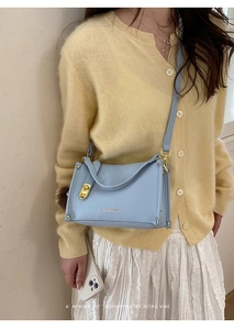 Detail of light blue crossbody bag with gold buckle and fuzzy ball charm on model
