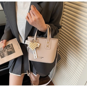 Chic beige bucket bag with pearl heart charm and lace detail held by a stylish model