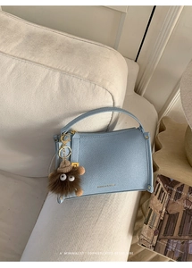 Detail of light blue lychee pattern handbag with a brown plush monster charm on a sofa