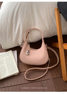 Pink lychee texture leather saddle bag with silver buckle on dark wooden floor