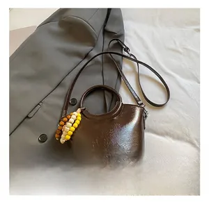 Detail of dark brown leather bucket bag with glossy finish and beaded accessory charm
