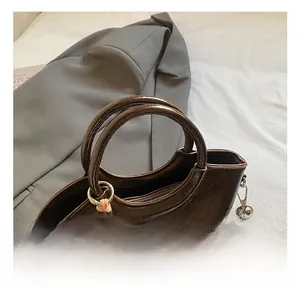 Detail of dark brown glossy bucket bag featuring integrated handle and bead charm