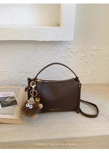 Detail of dark brown lychee leather bag with gold hardware and plush monster charm
