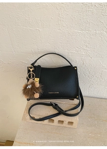Detail of black lychee texture handbag with gold lettering and brown plush monster charm